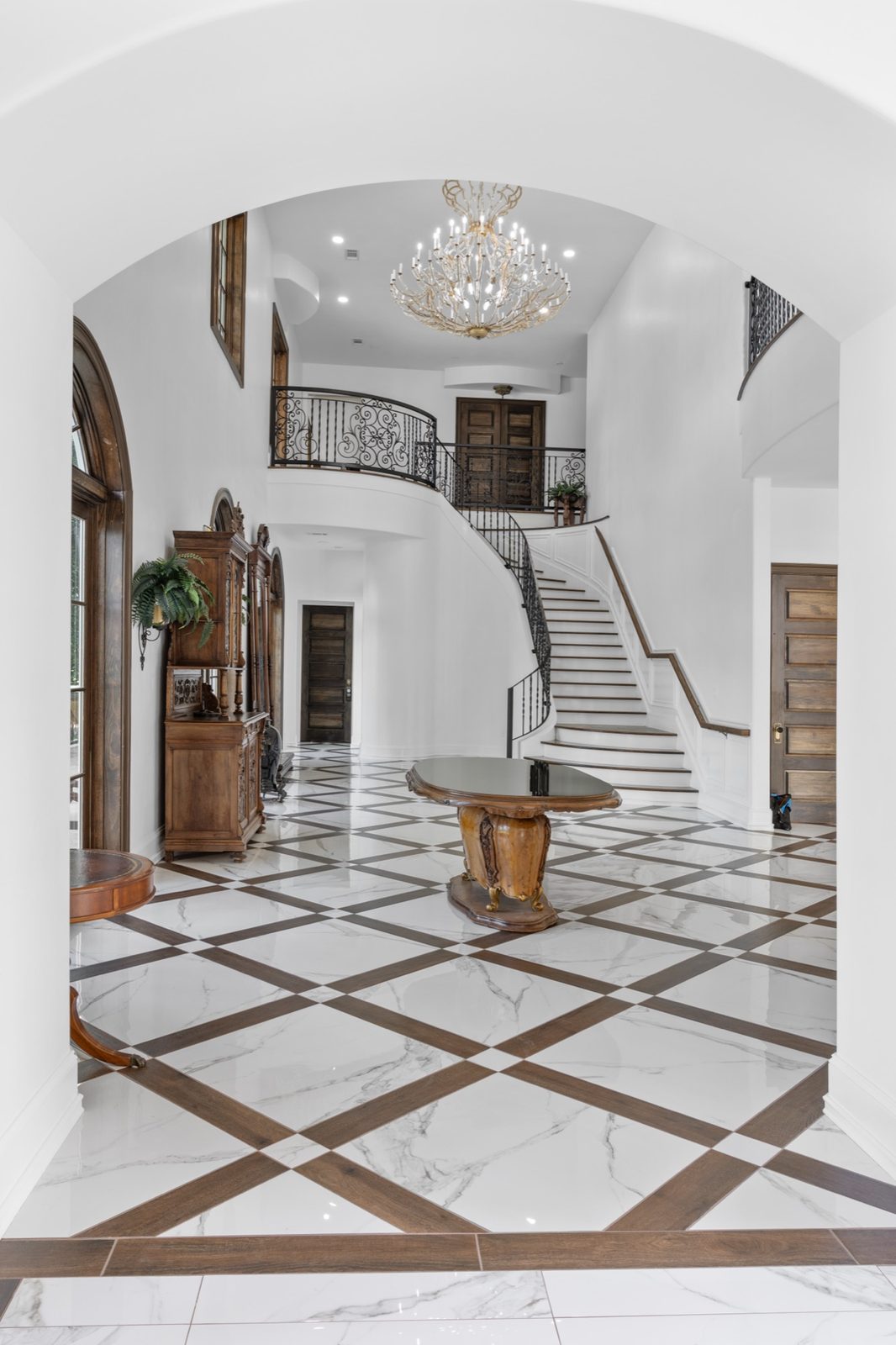 Grand foyer with chandelier, curved staircase and marble checkerboard floor